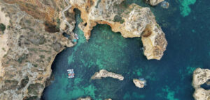 Aerial drone view of Ponta da Piedade with azure blue waters and golden cliffs dotted with green bushes.